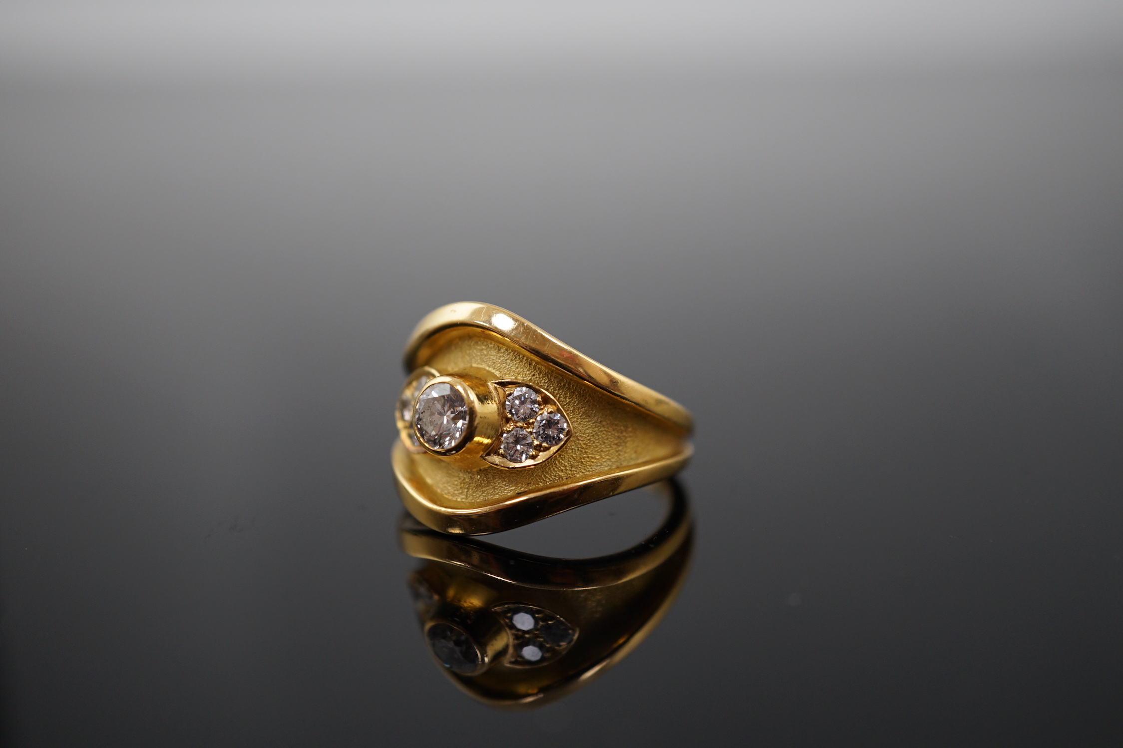 A 1990's part textured 18ct gold and collet set single stone diamond ring by Leo De Vroomen, with six stone diamond set shoulders, retailed by Boodle & Dunthorne